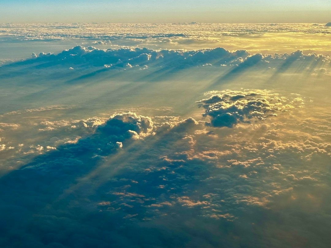 Golden hour sun rays pierce through layered clouds.